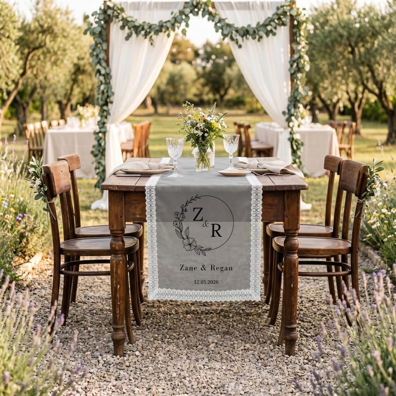 May include: A rectangular gray table runner with white lace trim, featuring a black circular floral wreath design with the initials Z & R, the names Zane & Regan, and the date 12.05.2026 printed in the center on a wooden table.