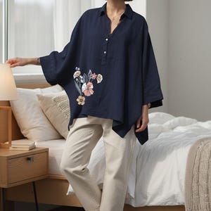 May include: A navy blue, oversized linen shirt with floral embroidery, paired with beige pants and white sneakers. The shirt features a button-down design and a relaxed fit, suitable for casual wear.