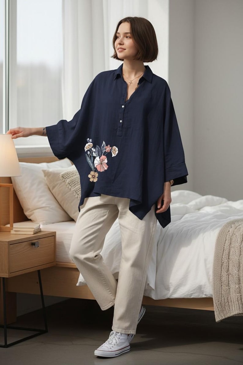May include: A navy blue, oversized linen shirt with floral embroidery, paired with beige pants and white sneakers. The shirt features a button-down design and a relaxed fit, suitable for casual wear.