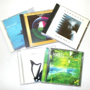 May include: A collection of five compact discs with various album art. The CDs feature a range of colors, including blue, green, and white. Album titles and artist names are visible, such as "Vangelis Themes" and "Kitaro".