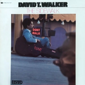 May include: Album cover for "The Sidewalk" by David T. Walker. The cover features a man in a blue suit sitting with a guitar case that has the word "Love" on it. The text "DONT WALK" is visible in the background.