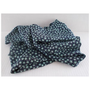 May include: A navy blue fabric with a repeating floral pattern in white and green. The fabric is folded and draped, showcasing the design. The flowers are small and evenly spaced across the material.