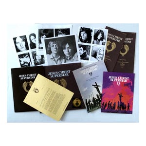 May include: A collection of vintage "Jesus Christ Superstar" memorabilia, including album covers, booklets, and promotional photos. The items feature black and white images of the cast and the musical's title in bold lettering. The color palette is primarily brown, black, and white.