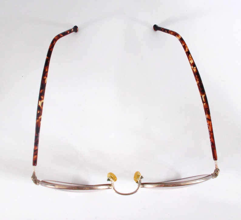 May include: Eyeglasses with a silver frame and tortoise shell arms. The glasses have a classic design with a curved browline and nose pads. The arms are a dark brown with lighter brown and tan spots.