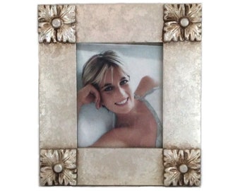 May include: A square, silver-toned picture frame with a photograph inside. The frame has a textured finish and decorative floral corner accents. The photograph features a smiling woman with short blonde hair.
