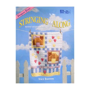 May include: A book cover titled "Stringing Along with Vanessa-Ann" featuring a quilt design. The quilt has squares with cat and heart motifs, hanging on a clothesline against a blue sky background. The author's name, Trice Boerens, is at the bottom.