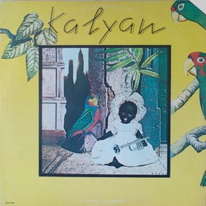 May include: Album cover with the title "Kalyan" in yellow script. The artwork features a doll in a white dress holding a trumpet, a colorful parrot, and a cityscape. Green parrots and foliage frame the image.