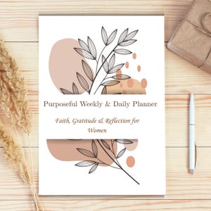 Puede incluir: Un planificador blanco con el texto "Purposeful Weekly & Daily Planner" y "Faith, Gratitude & Reflection for Women." La portada presenta un diseño botánico con acentos beige y marrón. También se ven un bolígrafo y un regalo envuelto.
