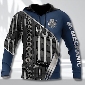 May include: A navy blue hoodie with a black hood and sleeves. The front features a toolbox design with wrenches and sockets, and the right sleeve has the word "MECHANIC" printed vertically. The hoodie includes a customizable name area.