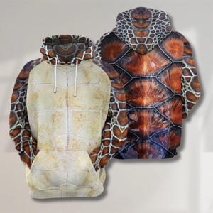Könnte beinhalten: Zwei Kapuzenpullover mit einem Schildkrötenpanzer-Design. Einer zeigt die Unterseite der Schildkröte in Beige und Braun, der andere die Oberseite des Panzers in Braun, Orange und Schwarz. Beide haben eine Kapuze und eine Vordertasche.