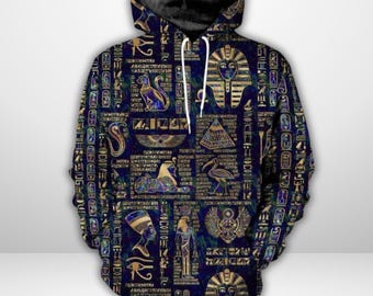 Pode incluir: Um moletom azul marinho com um padrão repetido de hieróglifos dourados e imagens egípcias. O design inclui máscaras de faraós, pirâmides e vários símbolos antigos. O moletom tem um capuz com cordão e um bolso frontal.