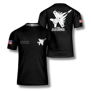 May include: Black t-shirt featuring a white graphic of a Boeing EA-18G Growler electronic warfare aircraft. The shirt has the American flag on the sleeve and a small patch on the chest. The back of the shirt also displays the aircraft graphic.
