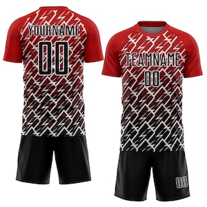 May include: Red and black soccer uniform set. The jersey has a red top with a white and black lightning bolt design. The shorts are black. The jersey has the text "YOURNAME" and "00" on the back and "TEAMNAME" and "00" on the front.