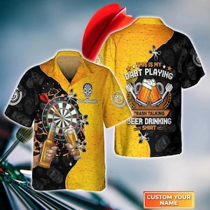 May include: A short-sleeved button-down shirt with a dartboard, beer, and the text "This is my dart playing, trash talking, beer drinking shirt." The shirt is yellow and black with a skull graphic and the option to customize the name.