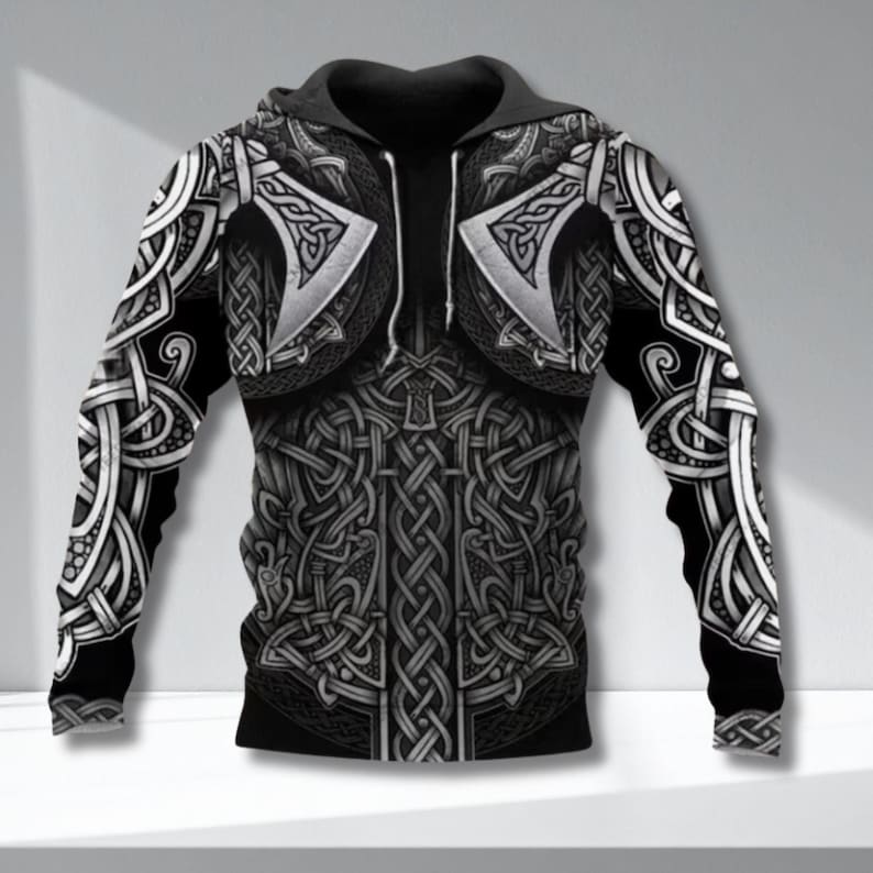 May include: Black and gray hooded sweatshirt with a detailed Viking armor design. The design features axes, intricate knotwork, and a textured appearance. The sleeves and torso are covered in the pattern, creating a bold, graphic look.