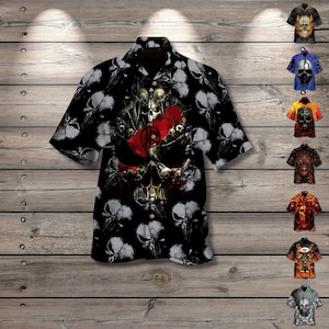 May include: Black button-down shirt with a skull and floral design. The shirt features a large skull graphic on the front, with smaller skull patterns throughout. Additional shirts with skull designs are displayed to the right.