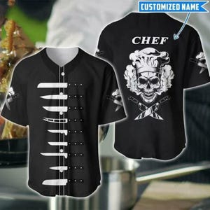 Puede incluir: Camiseta de béisbol negra con cuello blanco y cierre de botones. La parte delantera presenta una disposición vertical de cuchillos blancos. La parte trasera muestra una calavera con gorro de chef, cuchillos cruzados y la palabra "CHEF".