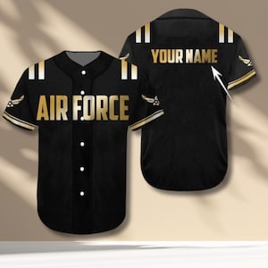 May include: Black baseball jersey with gold accents and the words "AIR FORCE" in gold lettering on the front. The back of the jersey has the words "YOUR NAME" in gold. The sleeves have gold trim and a military emblem.