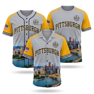May include: Three shirts featuring a gray and yellow color scheme with the text PITTSBURGH printed across the chest. The designs include a city skyline graphic, a bridge icon, and a small American flag patch on the sleeve of each garment.