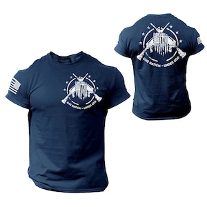 May include: Navy blue t-shirt with a white graphic on the front and back. The design features the American flag, crossed rifles, and the text "ONE NATION - UNDER GOD". The t-shirt has the American flag on the left sleeve.
