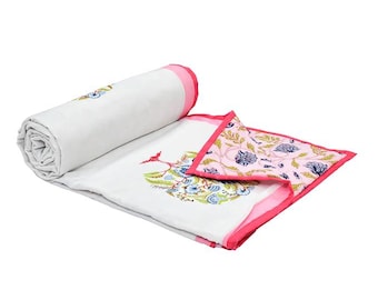 Könnte beinhalten: Eine weiße Baumwolldecke mit einem lebendigen floralen Blockdruckmuster in Blau- und Grüntönen. Die Decke ist teilweise aufgerollt und mit einer leuchtend rosa Bordüre versehen, die den hellrosa, floral gemusterten Unterstoff enthüllt.