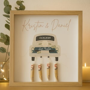 May include: A framed wedding keepsake featuring a vintage car illustration with the names "Kristin & Daniel" and the date 01.09.2025. The car has "Just Married" text and holds four rolled-up banknotes, each with the number 5.