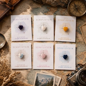 May include: Six rectangular cards labeled REISE SCHUTZSTEIN, each featuring a compass graphic and a small heart-shaped gemstone in purple, white, yellow, light blue, pink, or dark blue. The cards include the text: Wo auch immer du bist, ich begleite und beschütze dich.