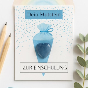 Op de afbeelding: Een wenskaart met de tekst "Dein Mutstein" en "ZUR EINSCHULUNG". De kaart heeft een blauw kegelvormig ontwerp met een hartvormige steen. De achtergrond heeft een lichtblauw stippenpatroon en een regenboog.