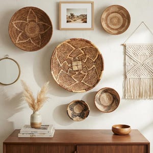 May include: A wall display featuring five woven baskets of varying sizes and patterns, a framed desert landscape print, a circular mirror, a cream-colored macrame wall hanging, a ceramic vase with dried grass, and a small wooden bowl on a cabinet.