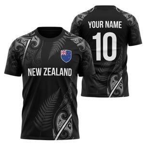 May include: Black New Zealand rugby jersey with white fern and tribal designs. The front displays "NEW ZEALAND" and a shield with the New Zealand flag. The back has "YOUR NAME" and the number "10" in white.