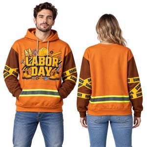 May include: An orange and brown hoodie featuring a Labor Day graphic with a hard hat, tools, and boots. The sleeves have yellow caution tape patterns with the word DANGER printed repeatedly. A reflective silver stripe runs across the front pocket.