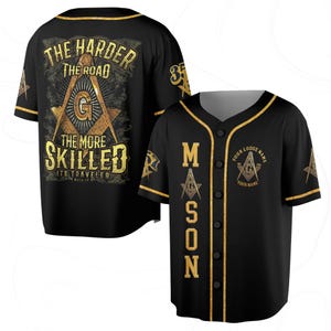 Könnte beinhalten: Schwarzes Baseball-Trikot mit goldenen Verzierungen und Akzenten. Auf der Vorderseite steht das Wort "MASON" in goldener Schrift, mit Freimaurersymbolen. Auf der Rückseite steht der Text "THE HARDER THE ROAD THE MORE SKILLED ITS TRAVELER".