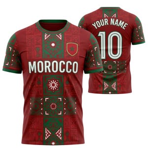 Peut inclure: Maillot de football bordeaux avec des détails verts et des motifs géométriques. Le devant affiche "MOROCCO" en lettres blanches et un écusson d'équipe. Le dos porte le numéro "10" et un espace pour un nom. Le maillot a un col rond et des manches courtes.
