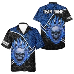 Puede incluir: Camisa de bolos de manga corta con una calavera y llamas azules, además de bolos. La camisa tiene un fondo negro con gráficos de bolas de bolos y patrones tribales azules. El texto "TEAM NAME" y "NAME" son visibles.