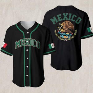 Könnte beinhalten: Schwarzes Baseball-Trikot mit grünen Zierleisten und dem Wort "MEXICO" auf der Vorderseite. Auf der Rückseite befinden sich das mexikanische Wappen und das Wort "MEXICO". Die Ärmel zeigen die mexikanische Flagge.
