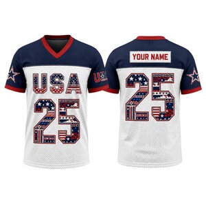 Peut inclure: Un maillot à manches courtes et col en V avec un corps en maille blanche et des épaules bleu marine. L'avant affiche USA et le numéro 25 dans un imprimé à motifs rouge, blanc et bleu. Le dos présente le numéro 25 et un encart YOUR NAME.