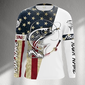 May include: Long-sleeved fishing shirt featuring a patriotic design with the American flag and a leaping fish graphic. The shirt has the words "FISHING" and "FISH" and the text "YOUR NAME" printed on the sleeves.