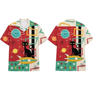 May include: A short-sleeve button-down shirt featuring a repeating pattern of black cats sitting on yellow and blue rockets, surrounded by planets, stars, and geometric shapes in red, teal, and cream colors with a classic collar and front buttons.