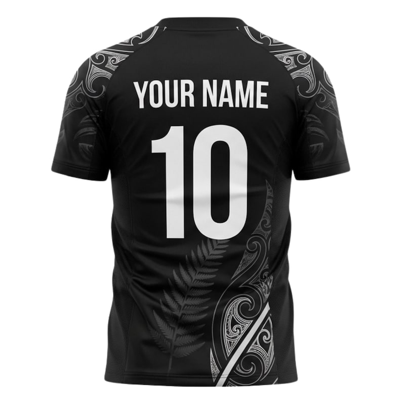 May include: Black athletic jersey with the text "YOUR NAME" above the number "10" in white. The jersey has decorative white patterns on the shoulders and sides, with a fern design. The jersey is short-sleeved.