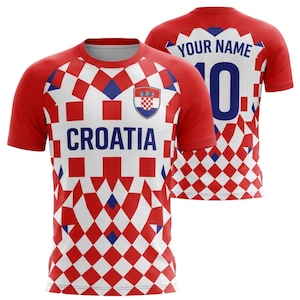 Pu&ograve; includere: Una maglia da calcio della Croazia rossa e bianca con un motivo a scacchi. La parte anteriore mostra "CROATIA" e lo stemma della squadra. La parte posteriore presenta "YOUR NAME" sopra il numero "10" in blu.