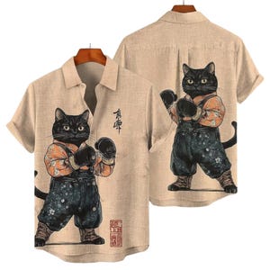 May include: Beige button-down shirt featuring a cartoon black cat wearing boxing gloves, an orange shirt, and denim overalls. The shirt has short sleeves and a collared neckline. Japanese text is printed on the shirt.