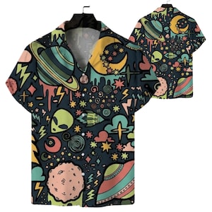 May include: A short-sleeve button-down shirt featuring a dark background with a colorful space-themed print. The pattern includes planets, crescent moons, alien faces, stars, lightning bolts, and flying saucers in shades of green, pink, and yellow.