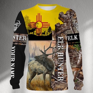 May include: Long-sleeved shirt with a yellow top and a design featuring an elk, trees, and the New Mexico state symbol. The sleeves have a camouflage pattern and the words "ELK HUNTER" and "YOUR NAME".