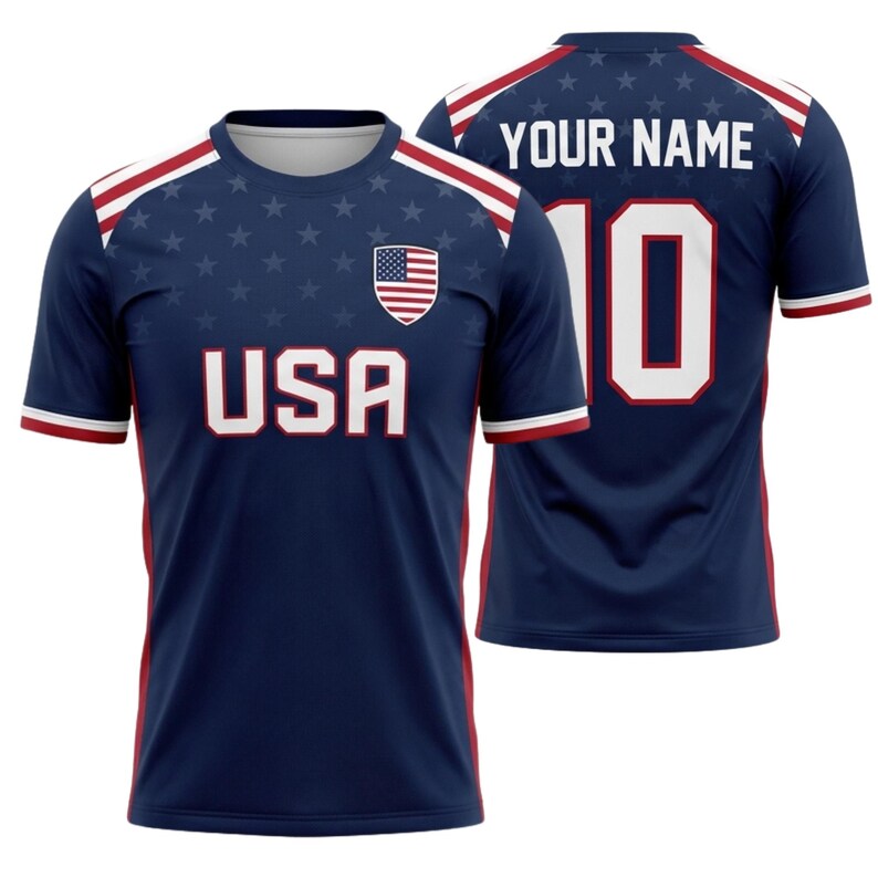 May include: A navy blue soccer jersey with white and red accents. The front features the word "USA" in white block letters, the American flag, and a pattern of stars. The back displays the number 10 and the text "YOUR NAME" in white.