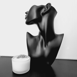 Puede incluir: Busto negro de cabeza y hombros de mujer, con un acabado liso y mate. Un peque&ntilde;o portavelas de cristal esmerilado con una rodaja de c&iacute;trico seco encima se encuentra frente al busto. El fondo es blanco.