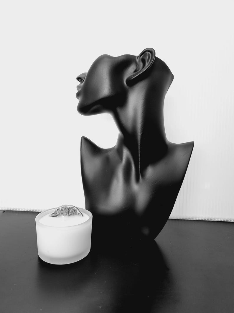 Puede incluir: Busto negro de cabeza y hombros de mujer, con un acabado liso y mate. Un peque&ntilde;o portavelas de cristal esmerilado con una rodaja de c&iacute;trico seco encima se encuentra frente al busto. El fondo es blanco.