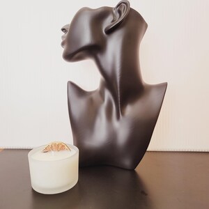 Puede incluir: Un busto de maniqu&iacute; negro con un acabado liso se encuentra junto a un peque&ntilde;o portavelas de cristal esmerilado. La vela es blanca y est&aacute; rematada con una rodaja de c&iacute;trico seco. El busto es un art&iacute;culo decorativo.