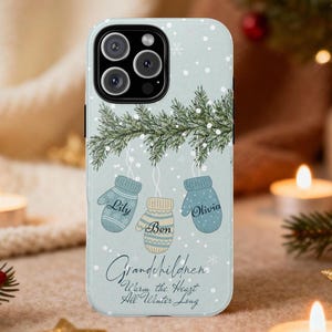May include: A light blue phone case featuring a winter design with falling snowflakes and a sprig of evergreen. Three hanging mittens are labeled "Lily", "Ben", and "Olivia". The text reads "Grandchildren Warm the Heart All Winter Long."