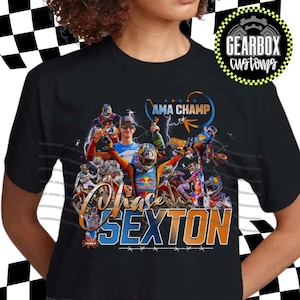 Puede incluir: Camiseta negra con un gráfico temático de motocross. El diseño incluye el nombre "Chase Sexton" y las palabras "AMA Champ". El gráfico presenta imágenes de un corredor, un logotipo de Red Bull y un logotipo de Gearbox Customs.