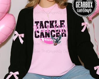 Puede incluir: Una sudadera rosa con el texto "Tackle Pink Out Cancer" y un gráfico de águila. La sudadera se usa con una rebeca negra adornada con lazos rosas. La persona lleva vaqueros azules y zapatillas a cuadros.